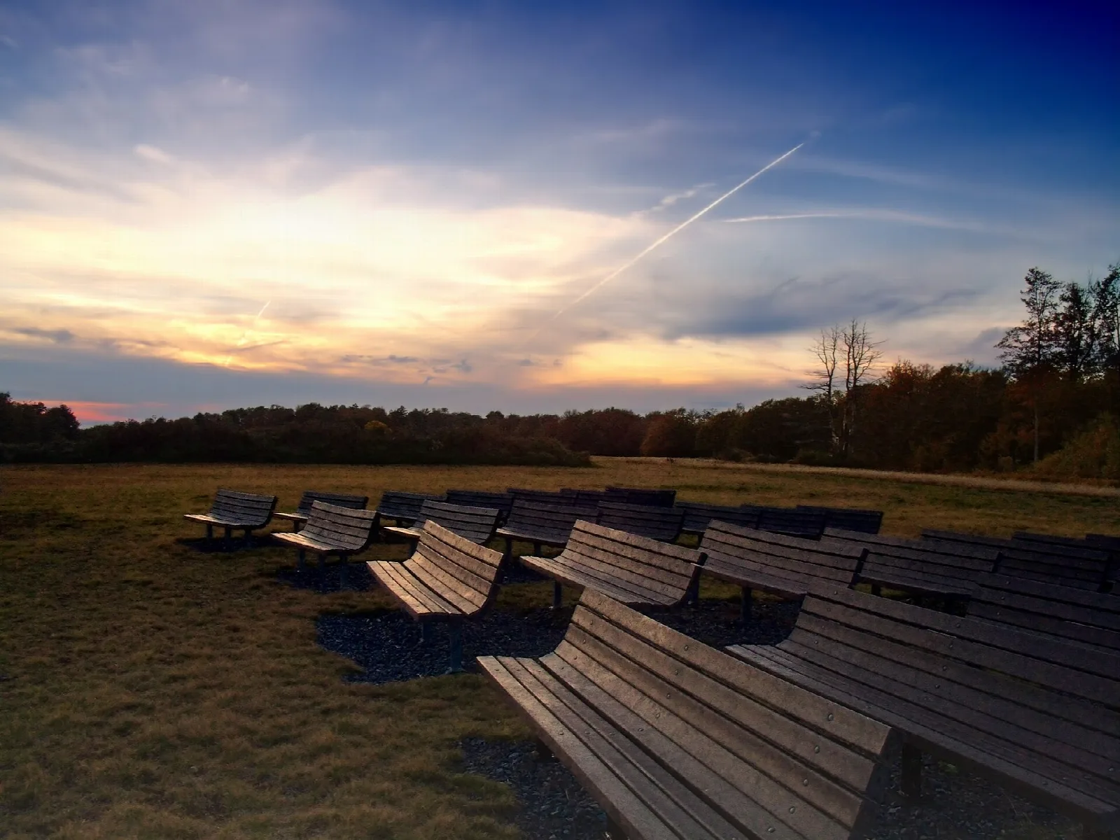 Rows of benches in an open field under a sunset sky
