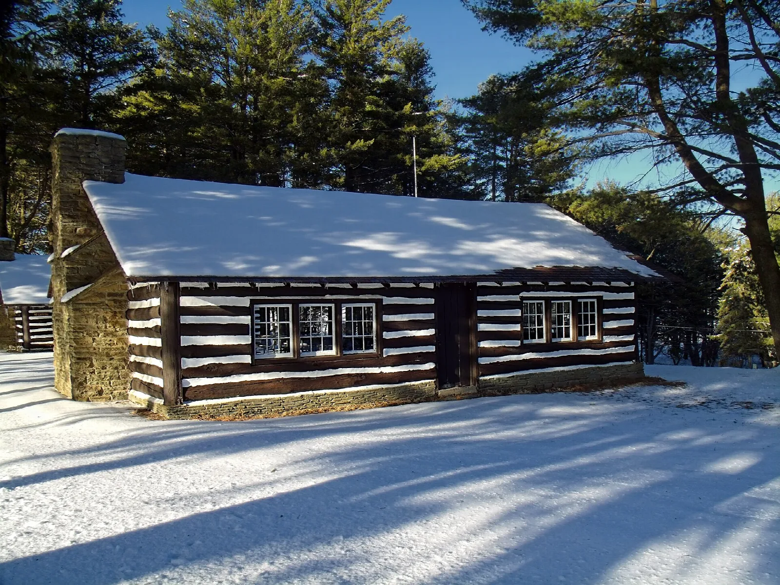 Log and stone pavilion with a snowy roof among pines