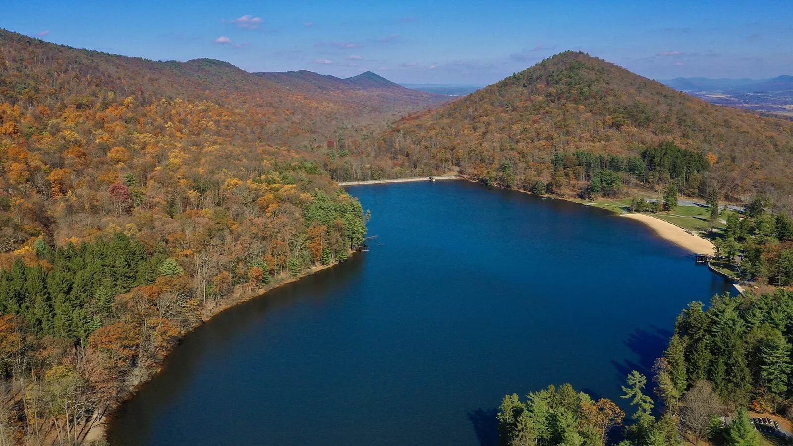 Blue lake among forested hills with fall color and a sandy beach