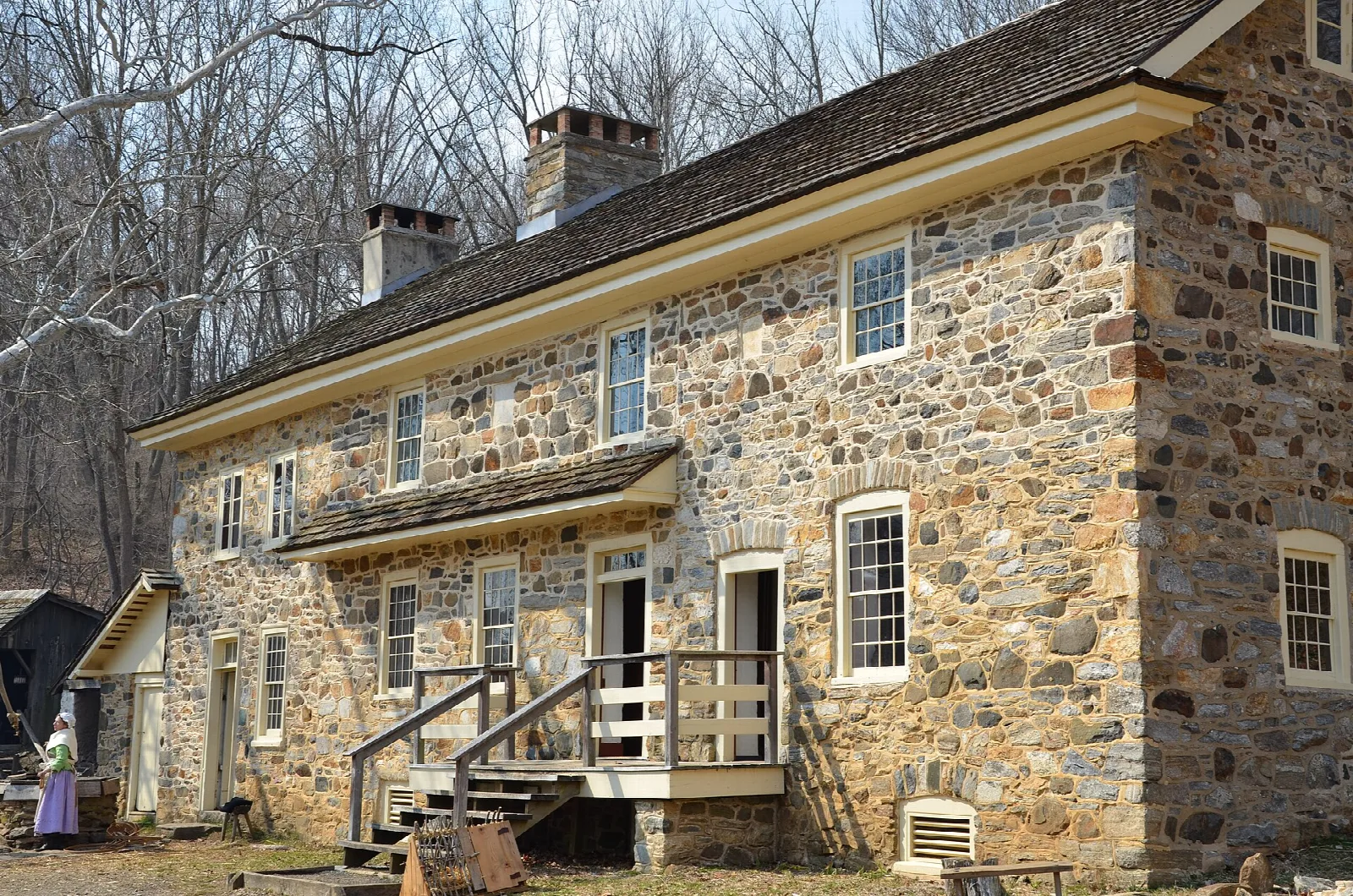 Large stone farmhouse with a covered porch in bare trees