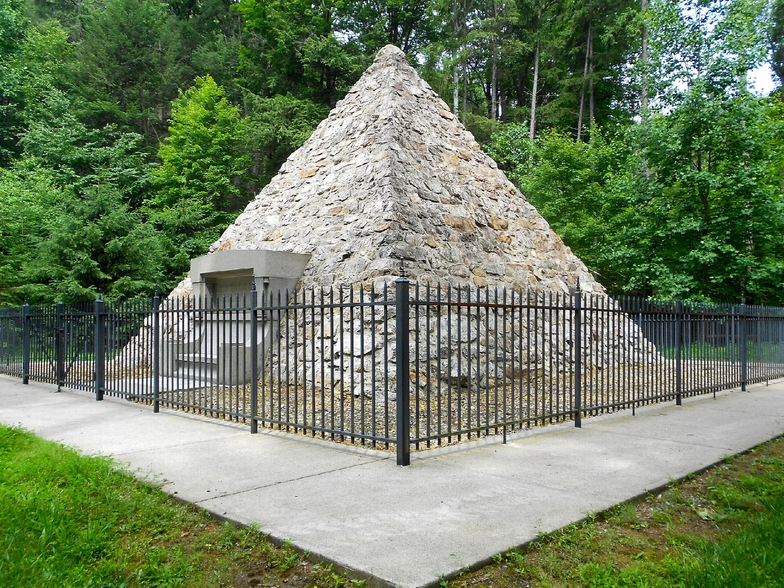 Stone pyramid behind an iron fence on a green lawn