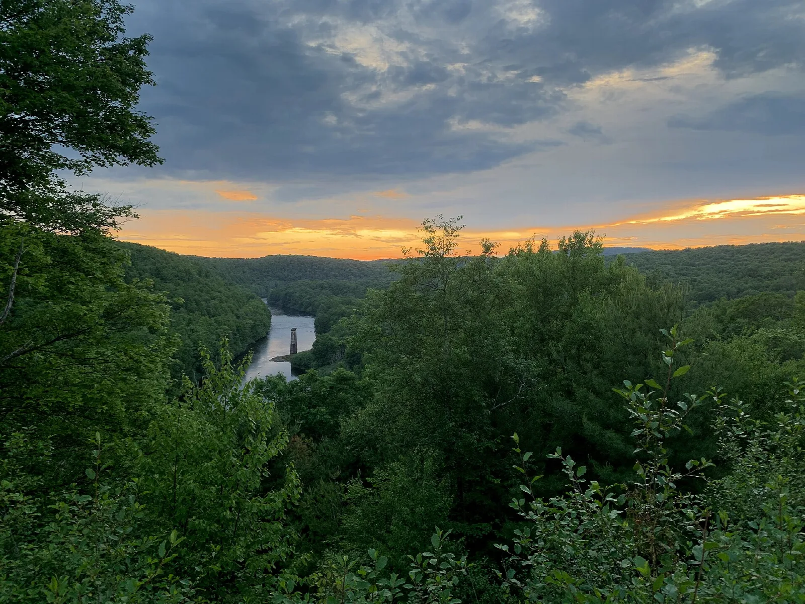 Forested gorge at sunset with a white dam in the distance