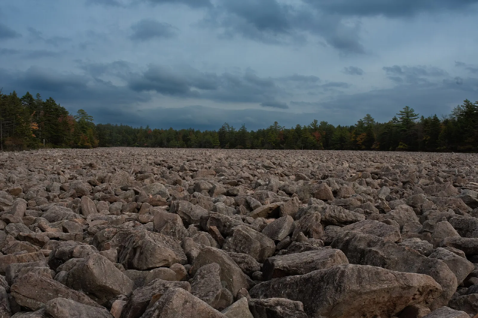 Dark boulder field under stormy clouds with forest behind