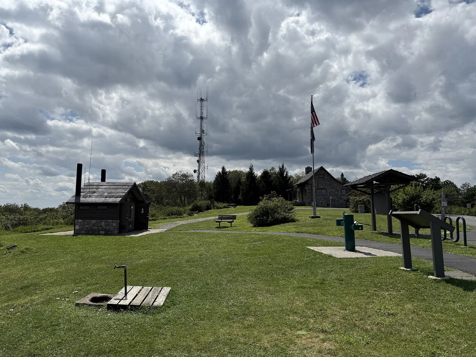 Grassy summit with small log buildings, a flagpole, and towers under a cloudy sky