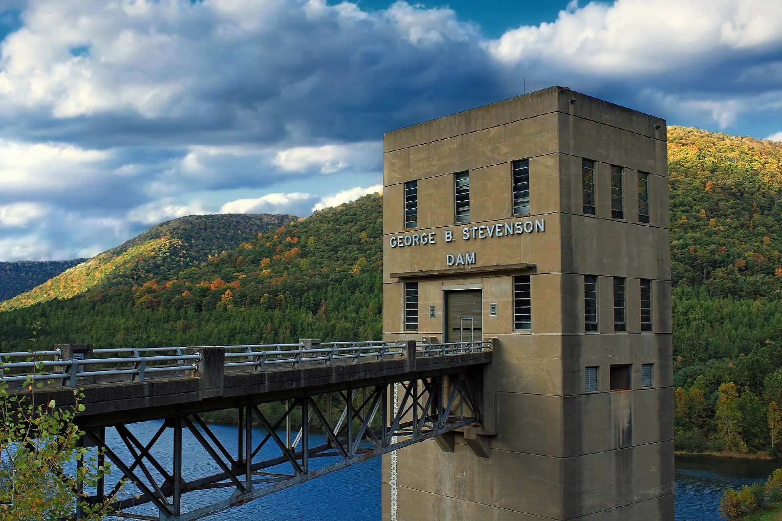 Concrete dam tower and walkway with forested hills behind