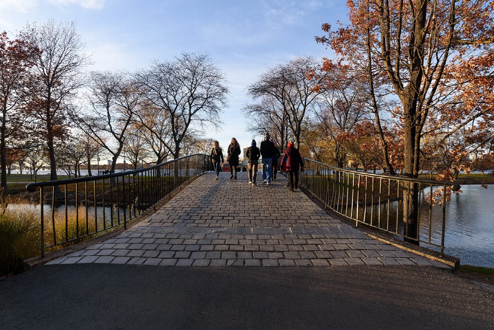 A brick footbridge with walkers under bare and orange autumn trees