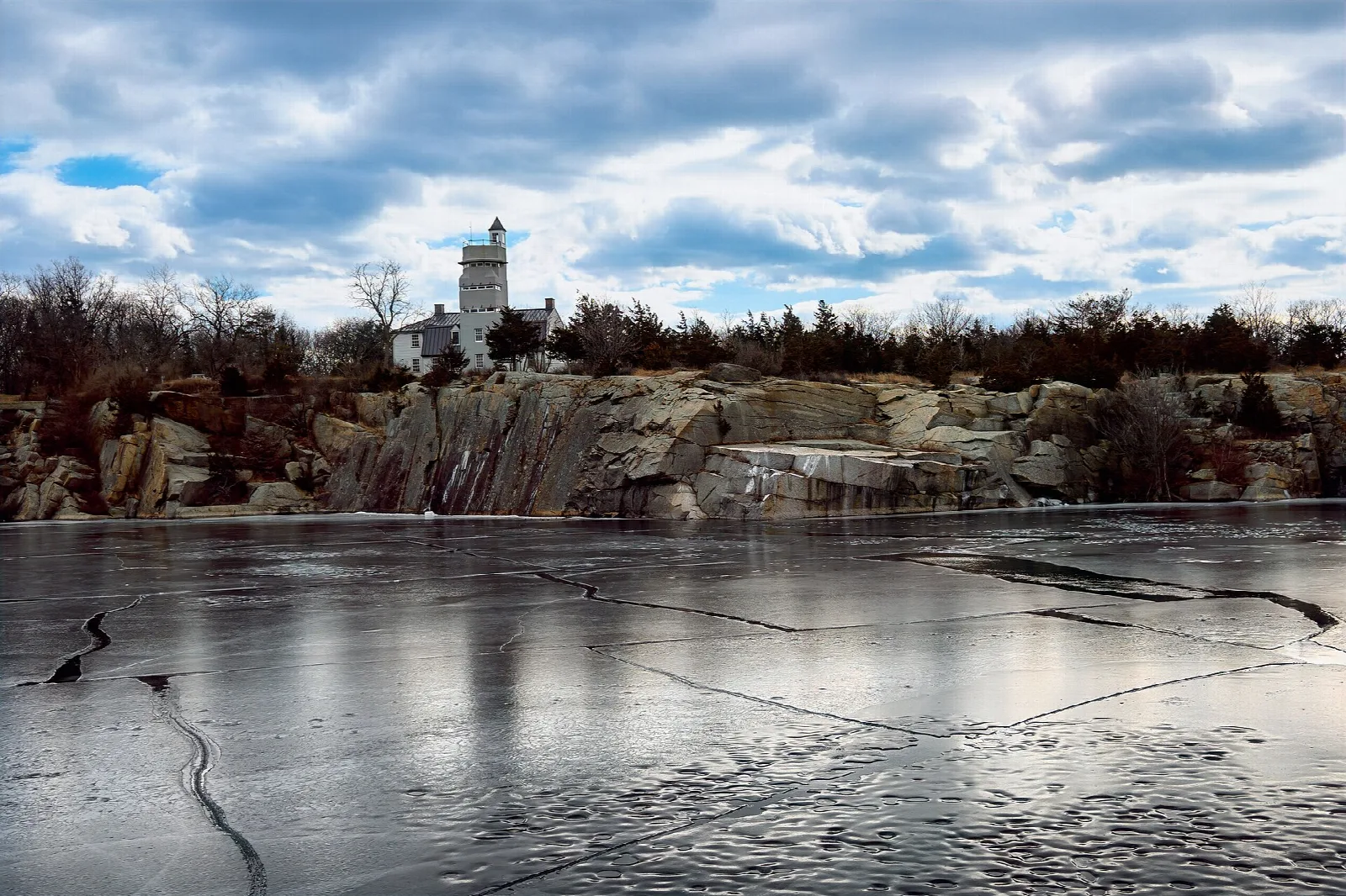 Ice-covered quarry water with a lighthouse-like building beyond the rocks