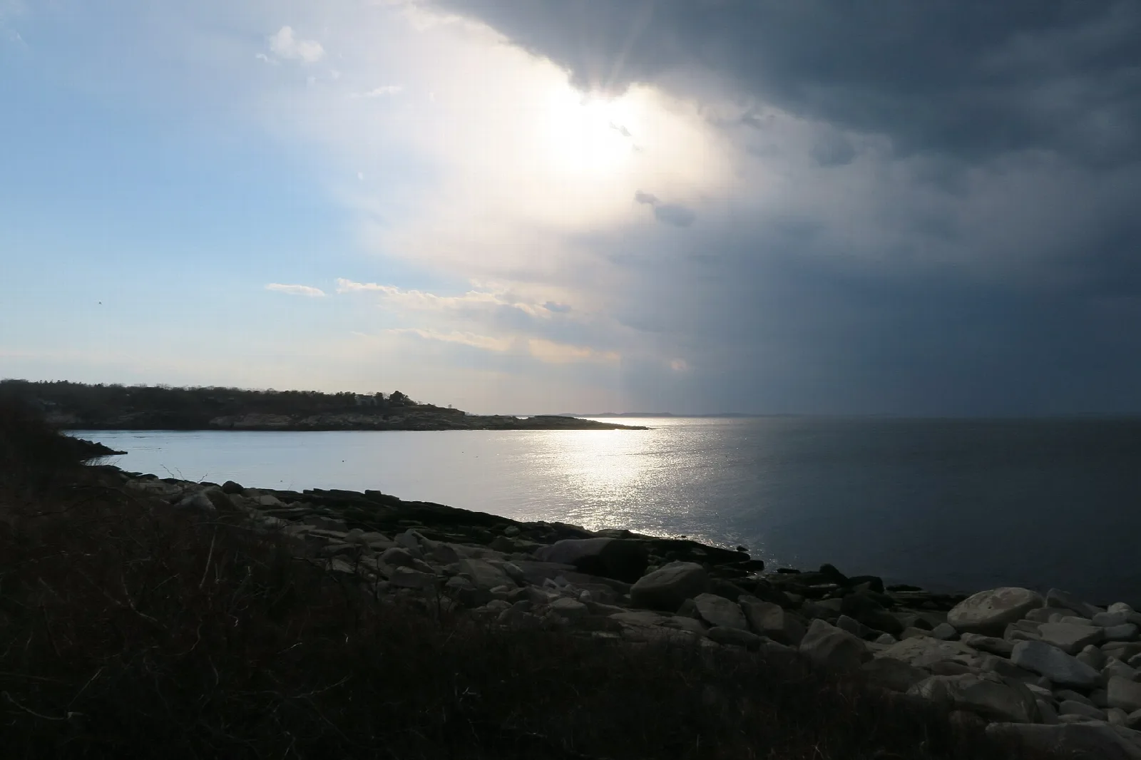 Sunlight on the sea beside a dark rocky shore
