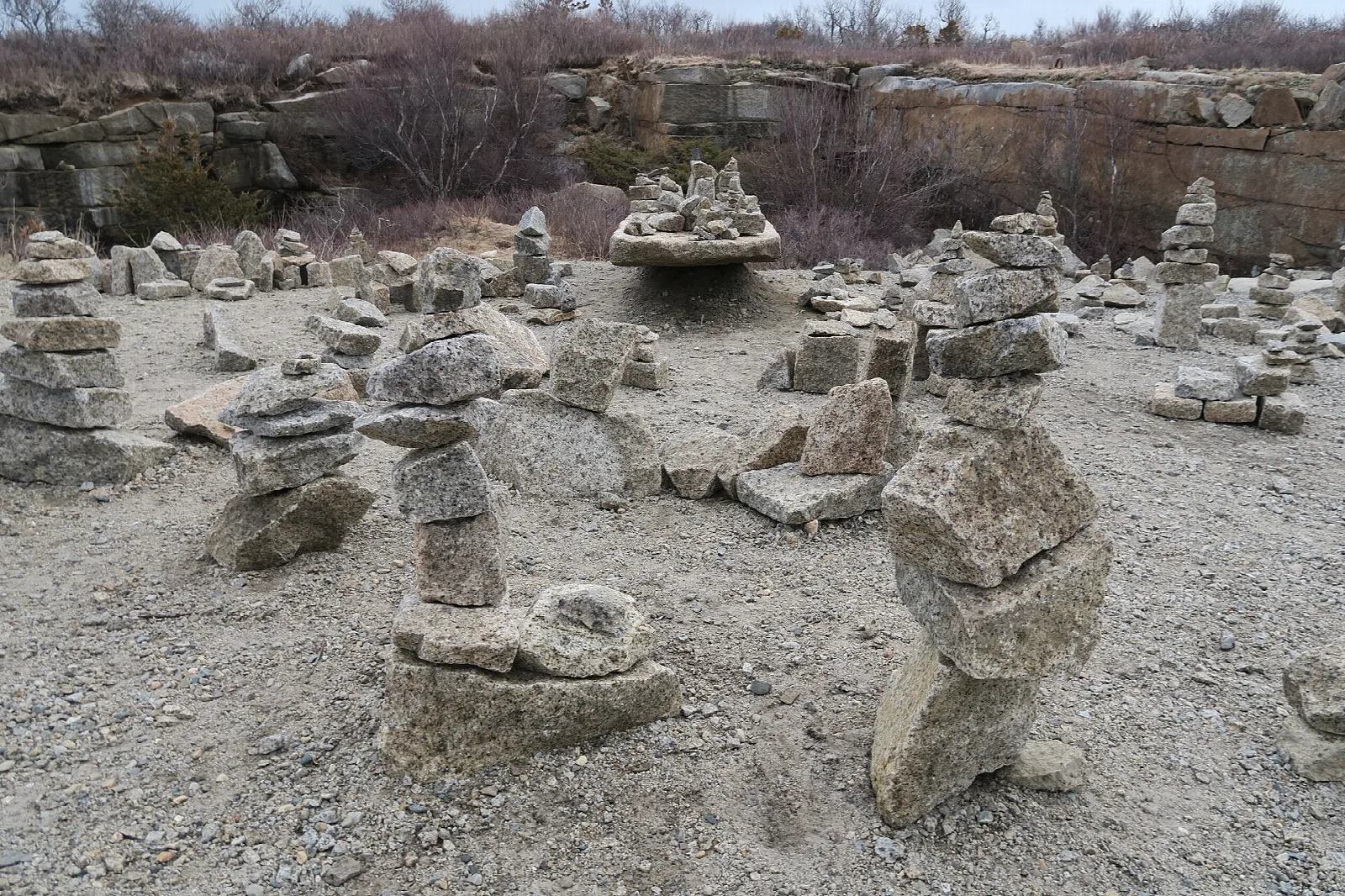Many small stacked stone cairns on a gravel quarry floor