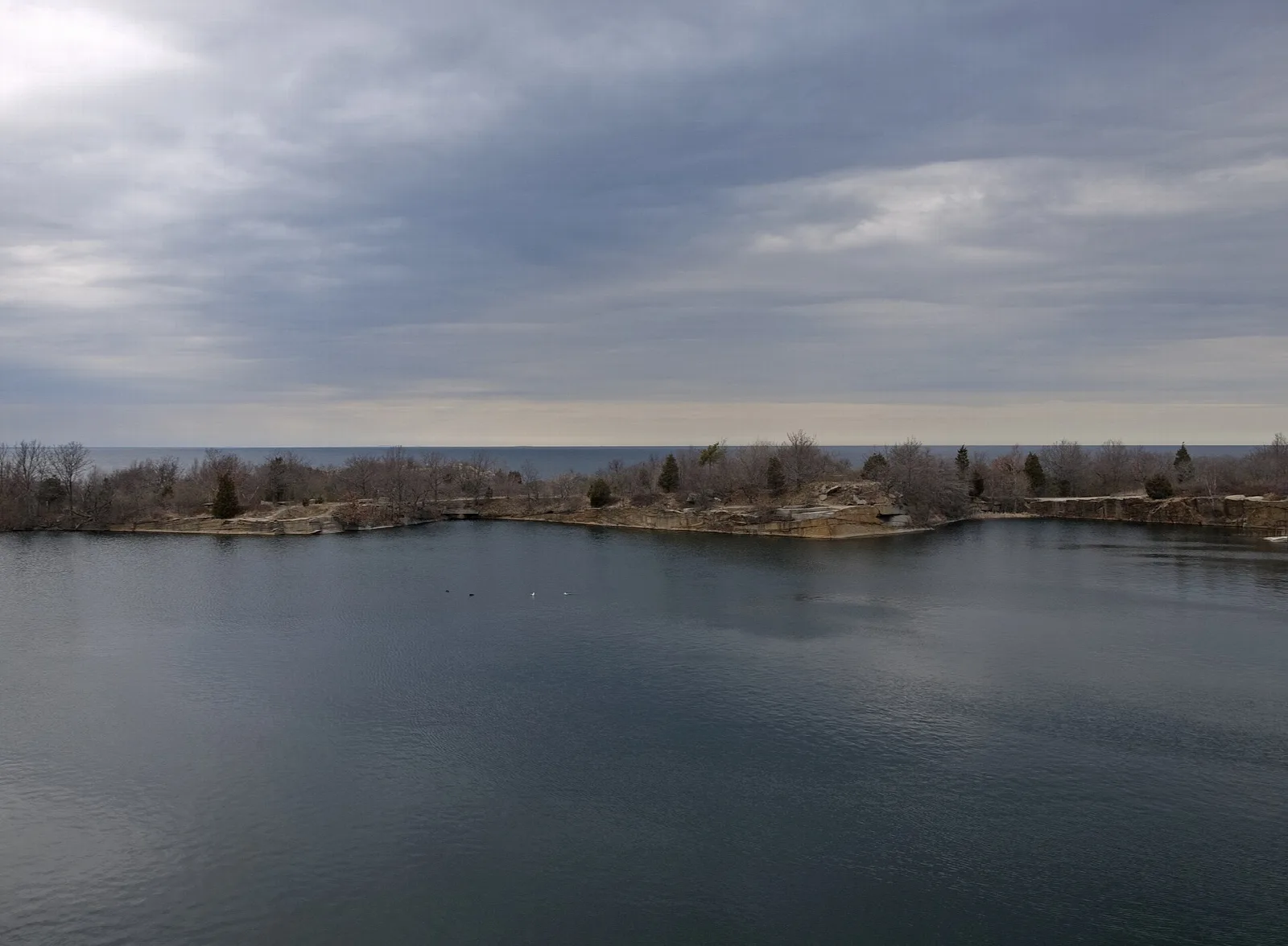 A flooded quarry with a low wooded shoreline across the water