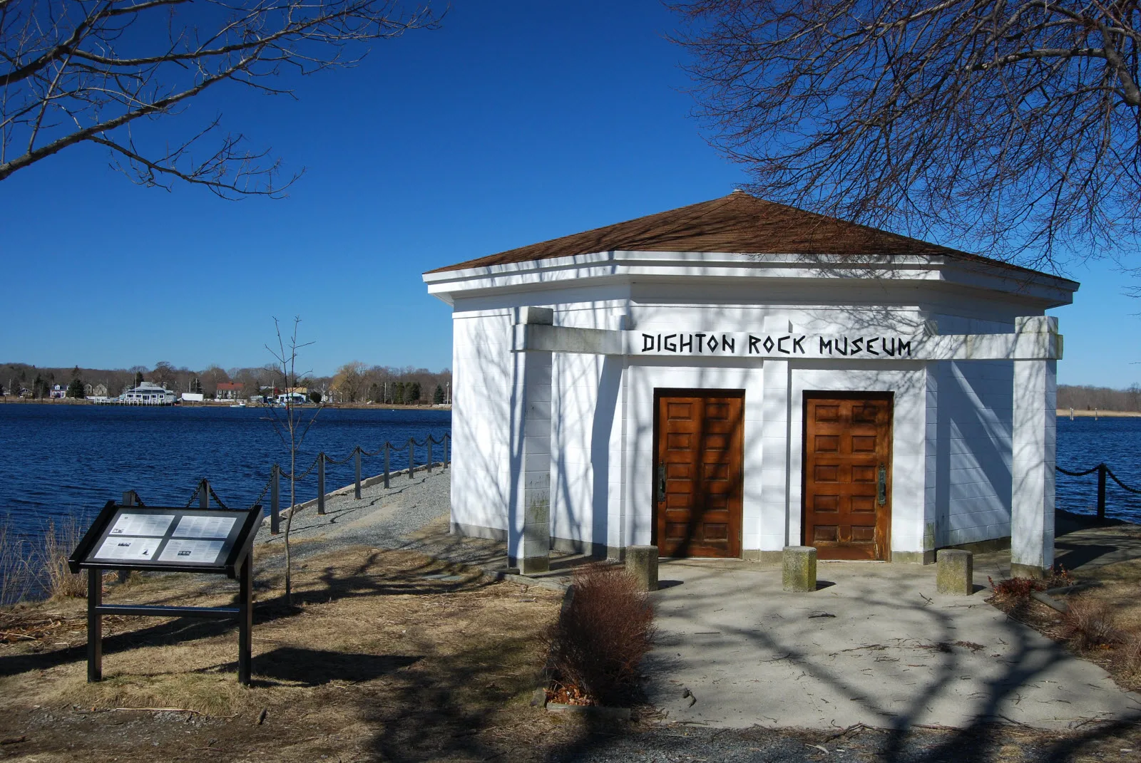 A small white round building labeled Dighton Rock Museum beside the water