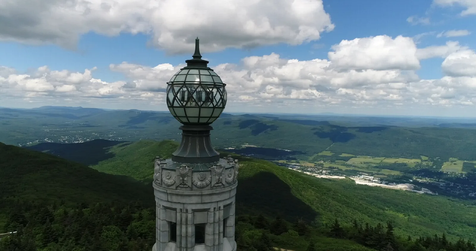 A lantern-topped stone tower above a wide green valley and hills under clouds