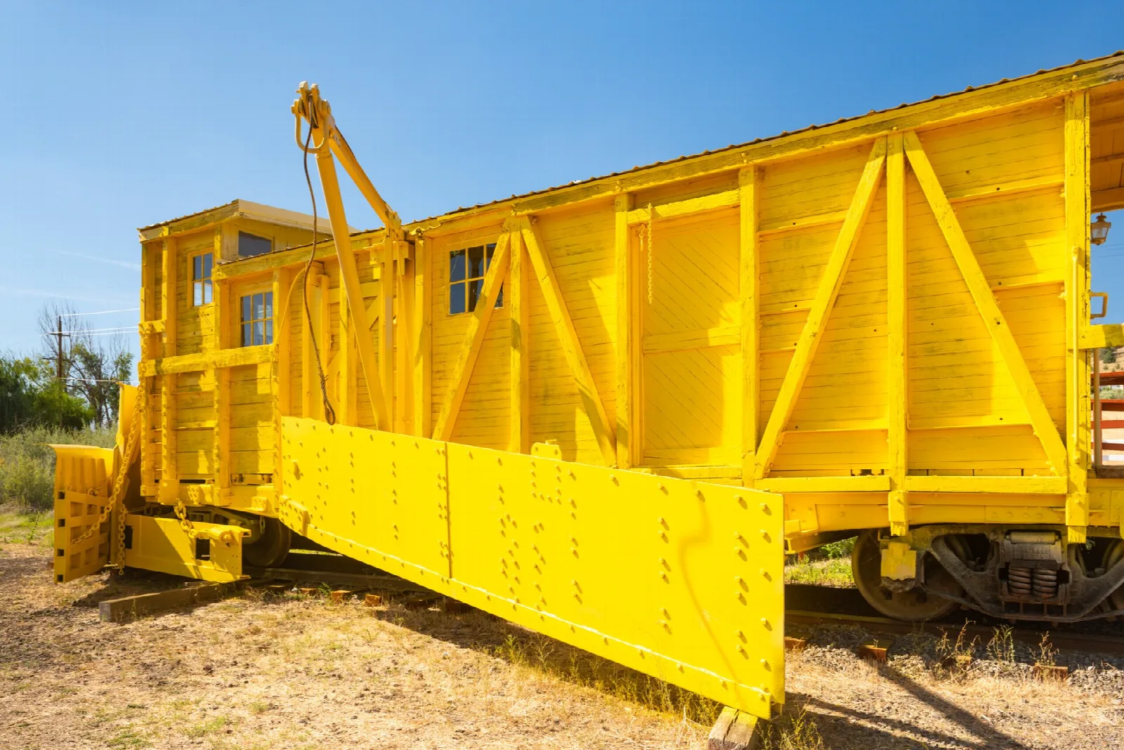 Yellow plow rail car with a boxy cab beside the track