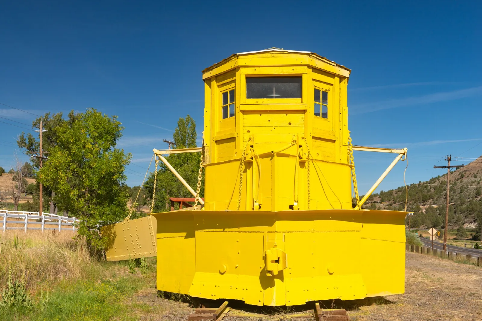 Front of a yellow snow-plow rail car on a track with brush behind