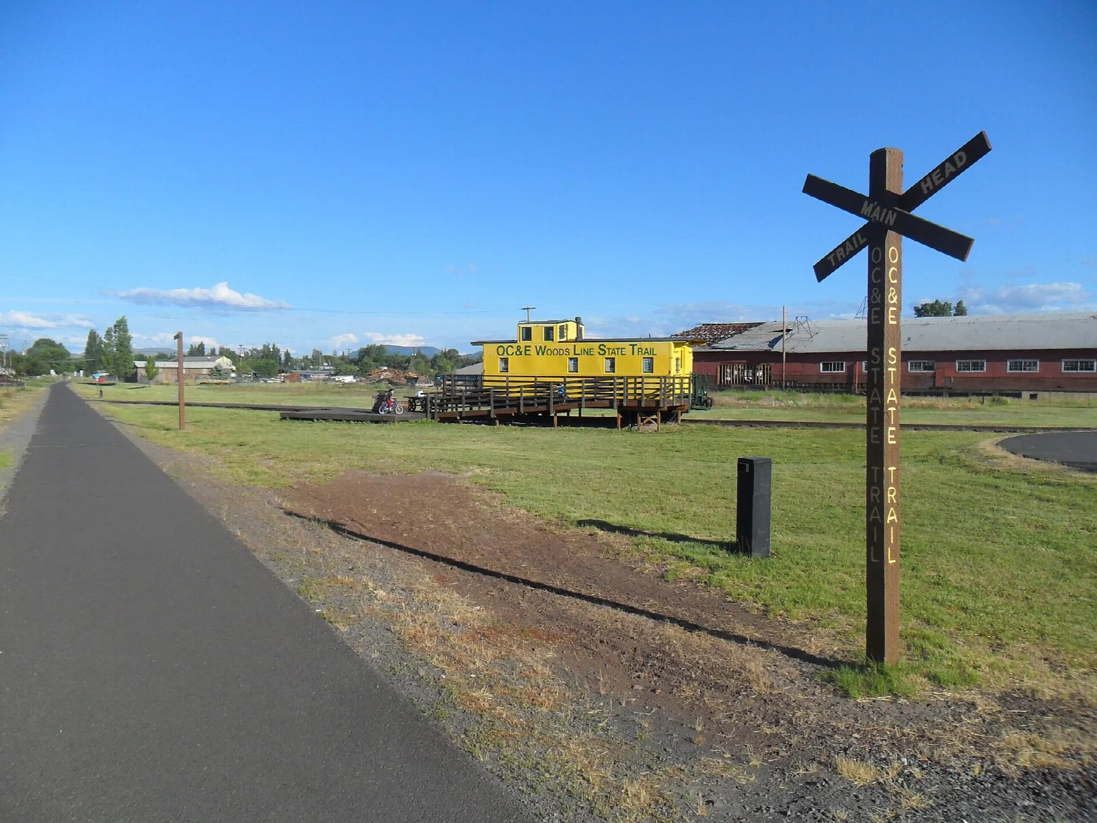Paved trail beside a grassy field with a yellow caboose in the distance