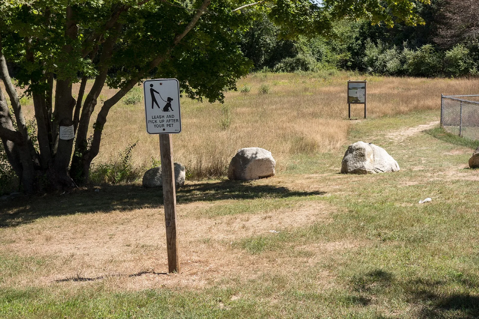 A grassy field with boulders, a tree and a small trail sign