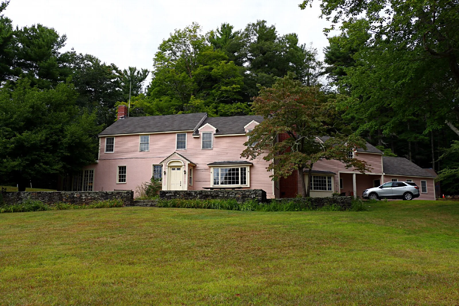 A pink two-story house across a lawn, with trees behind