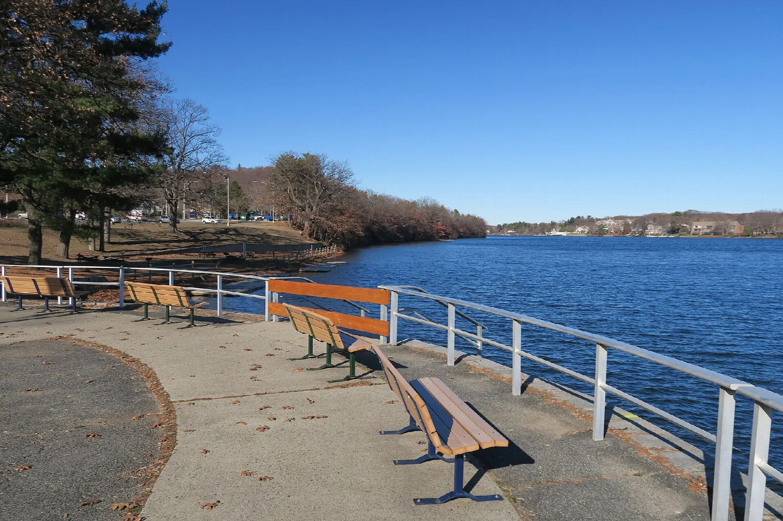 Blue lake water behind a railing and benches on a paved walkway