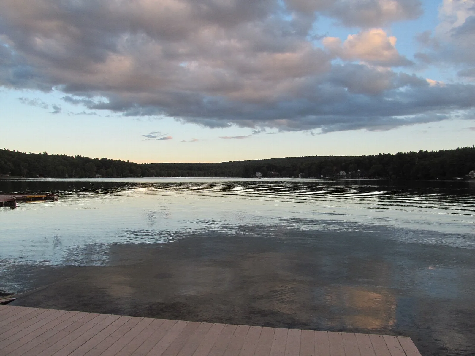 A calm lake at dusk with pink clouds and a wooden dock in the foreground