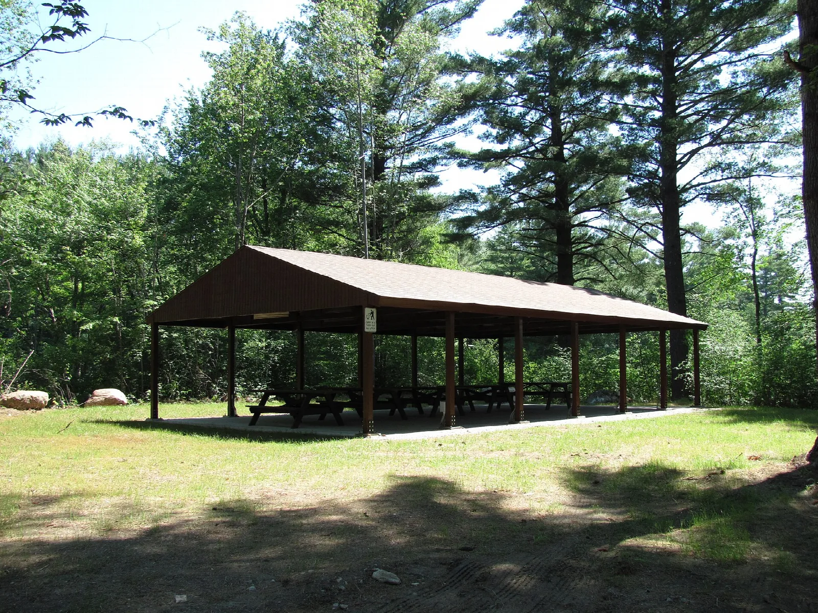 A brown-roofed picnic shelter on a lawn among pines