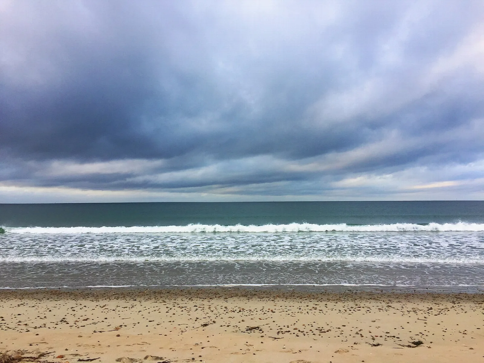A wide sandy beach with surf under dark clouds
