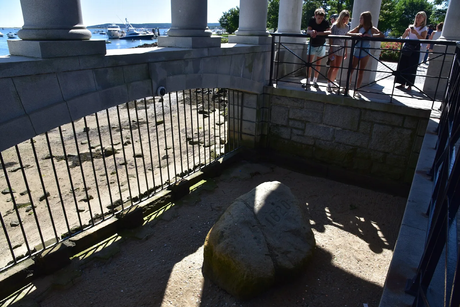 A boulder inside a railed pit beneath the portico, with visitors looking down