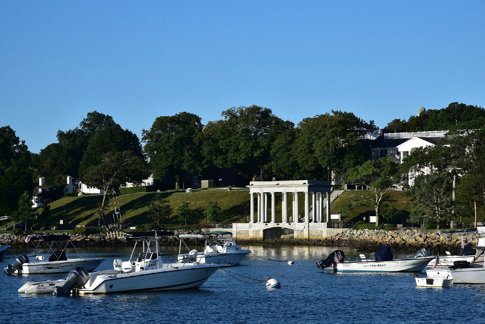 A harbor with moored boats and the columned portico among green trees beyond