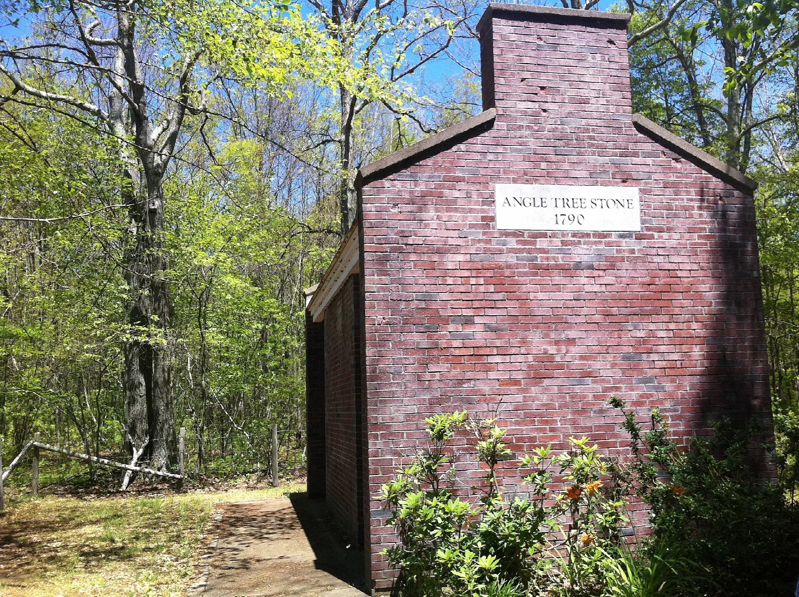 Small brick shelter with a sign above its door, among trees