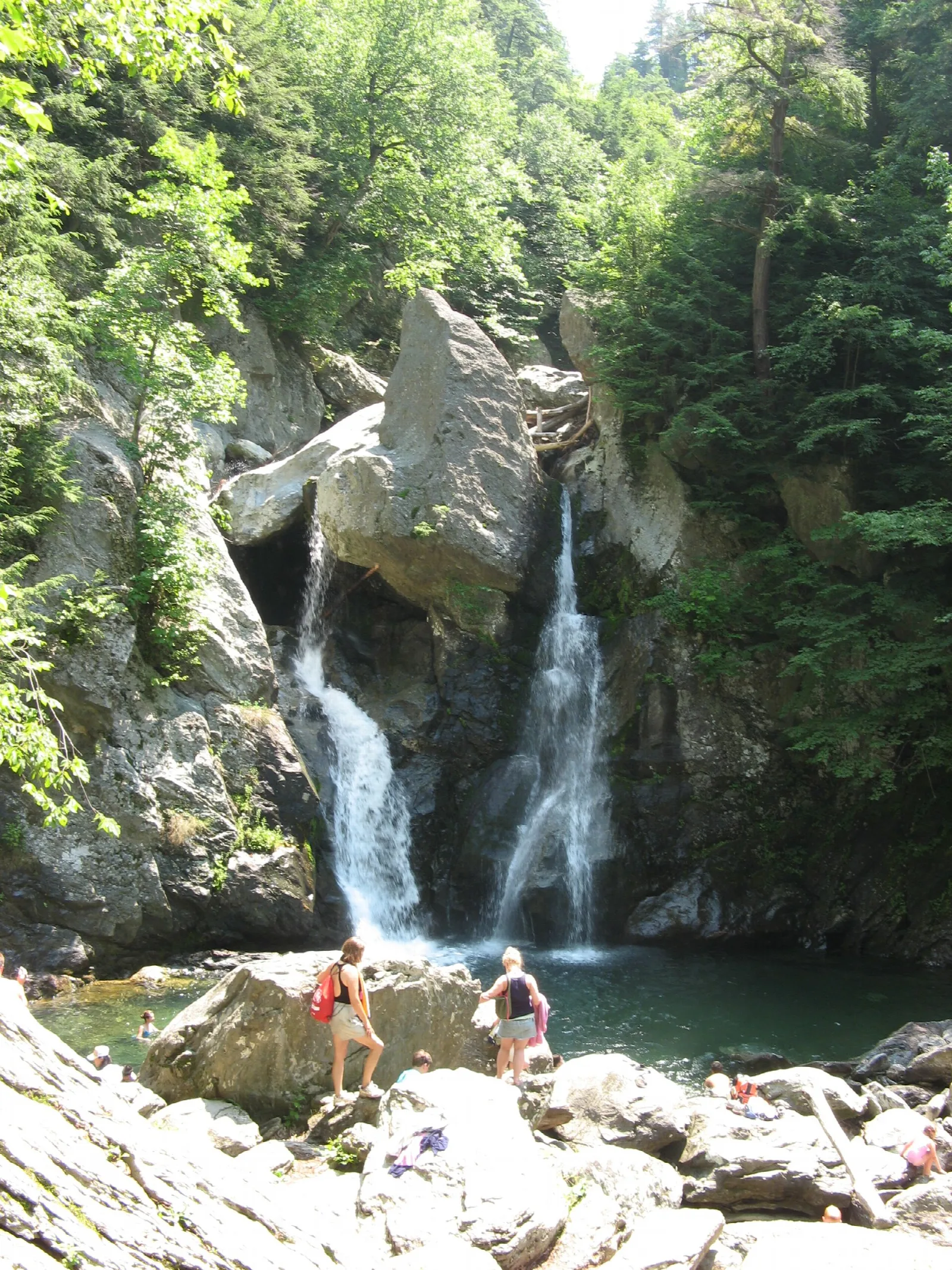 Two-stage waterfall between rock walls into a pool, with a few people on rocks below