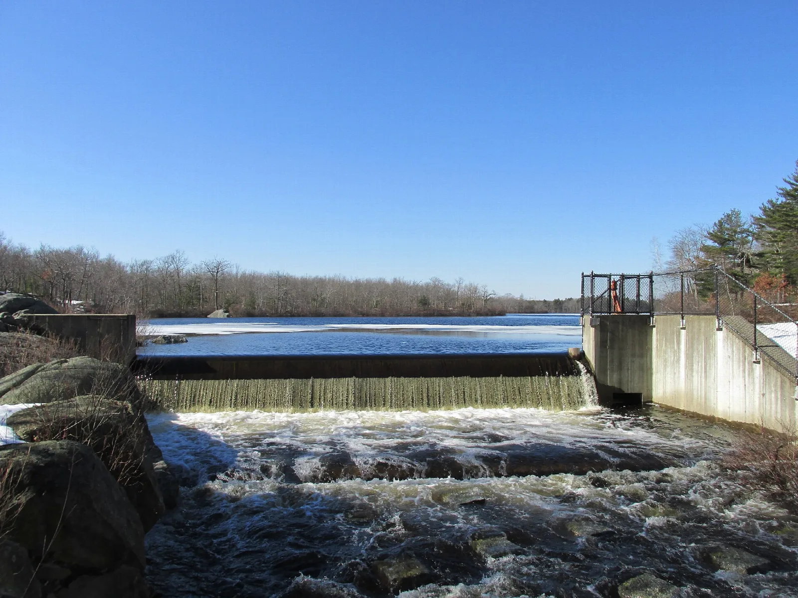 Water spilling over a low dam into a stream beside the pond
