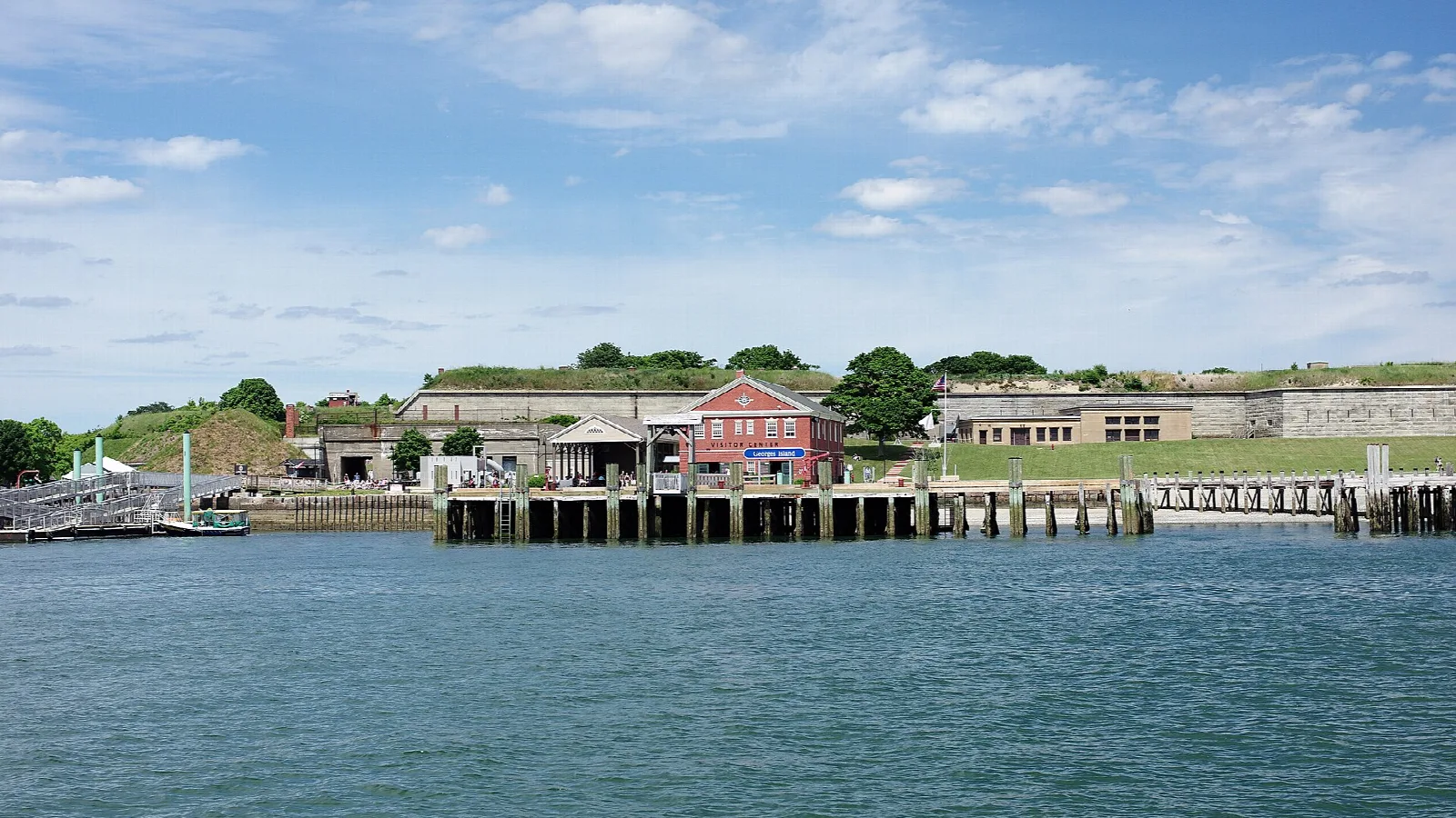 Dock and red brick building with a grassy fort wall behind, seen from the water