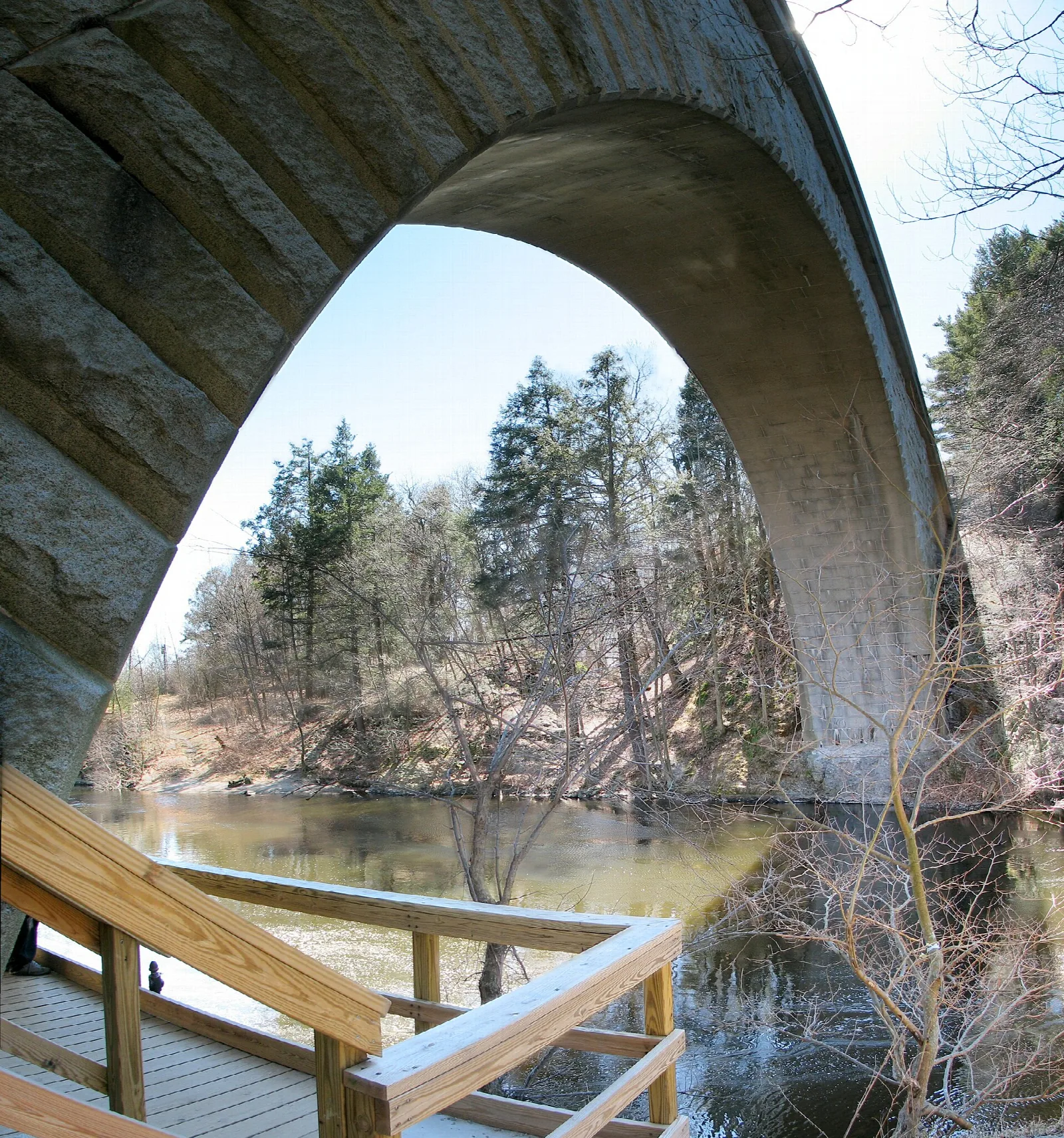 Stone bridge arch framing a river and bare trees, with a wooden deck in front