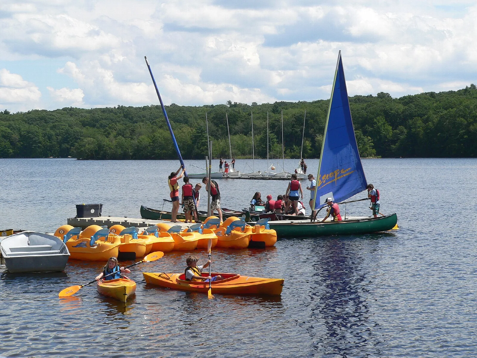 Sailboat and orange kayaks on a reservoir with forest behind