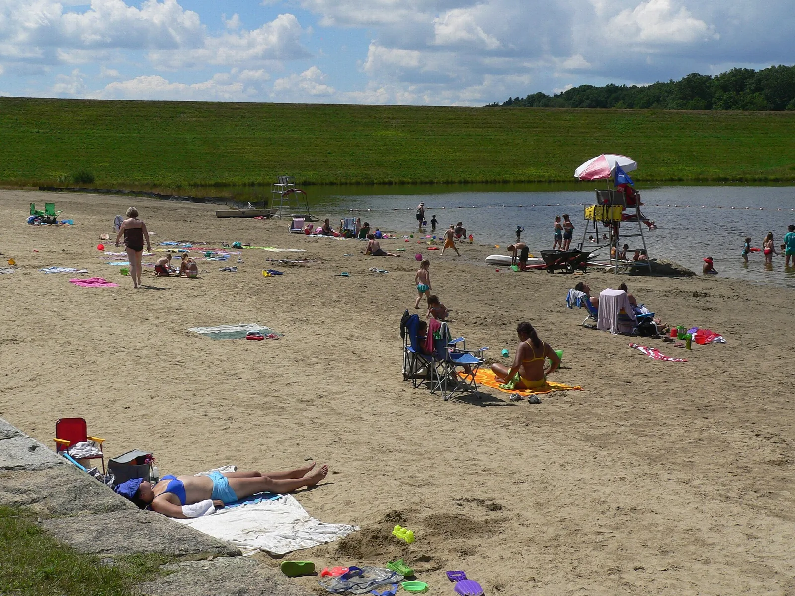 Sandy swimming beach below a grassy dam with people sunbathing