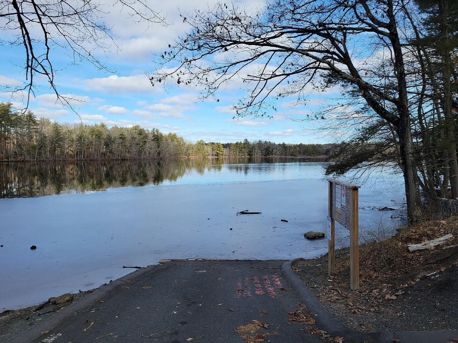 Calm river reservoir with a boat ramp, a sign and trees along the shore