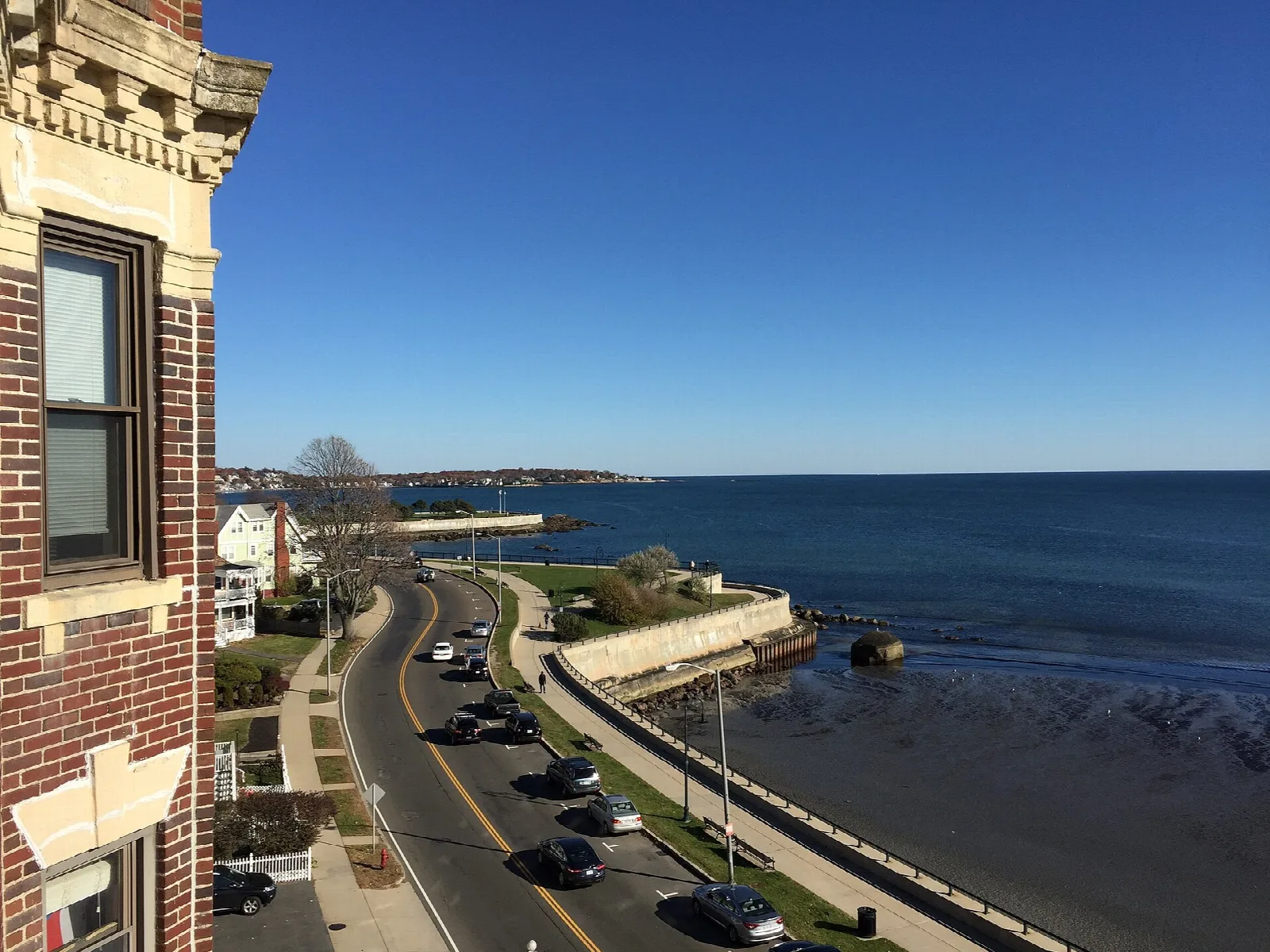 Coastal road along a seawall with blue ocean beyond a brick building