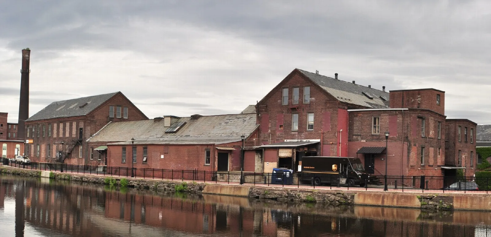 Red brick mill buildings along a still canal under a cloudy sky