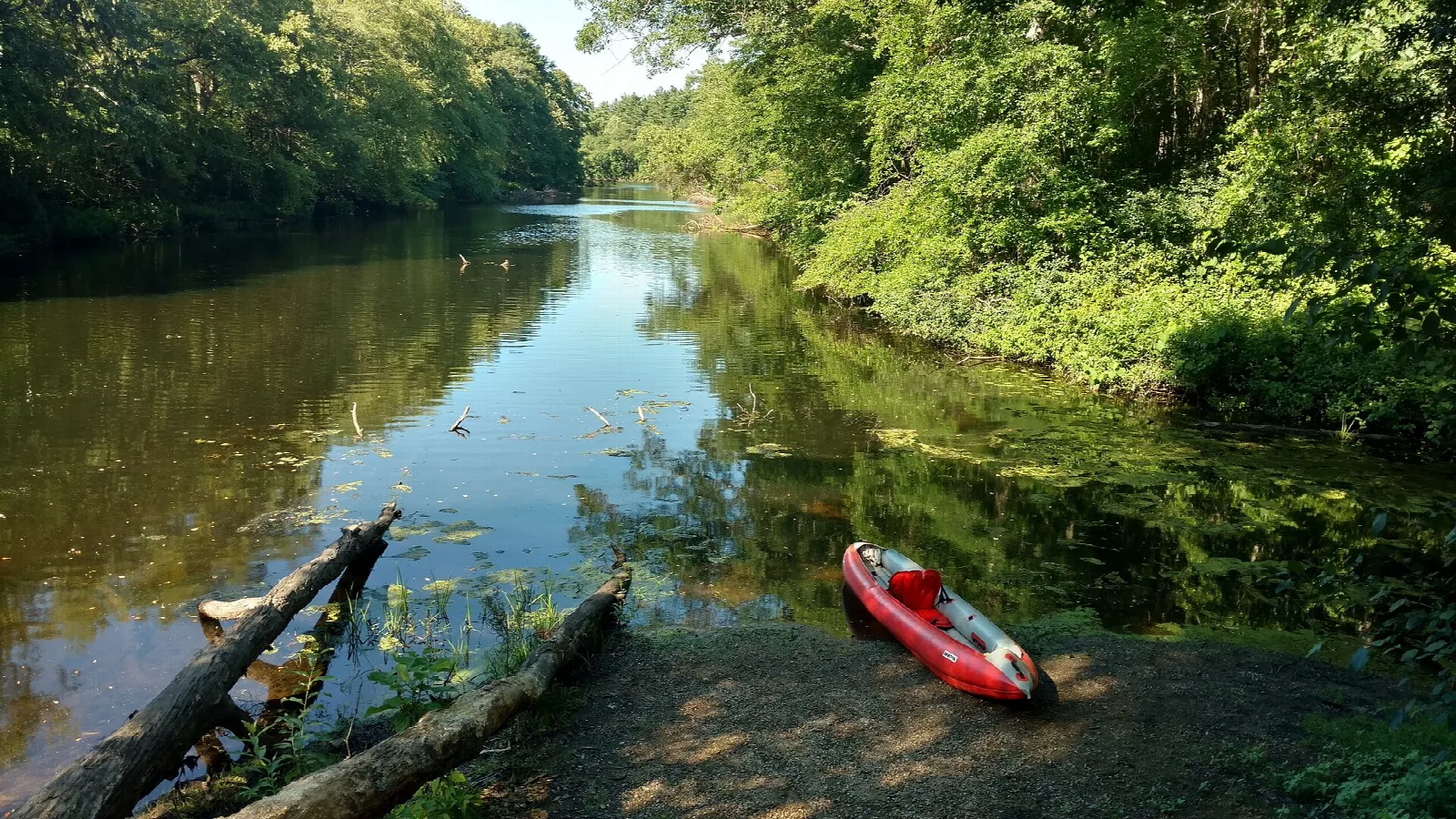 Calm river with a red kayak on a shady bank