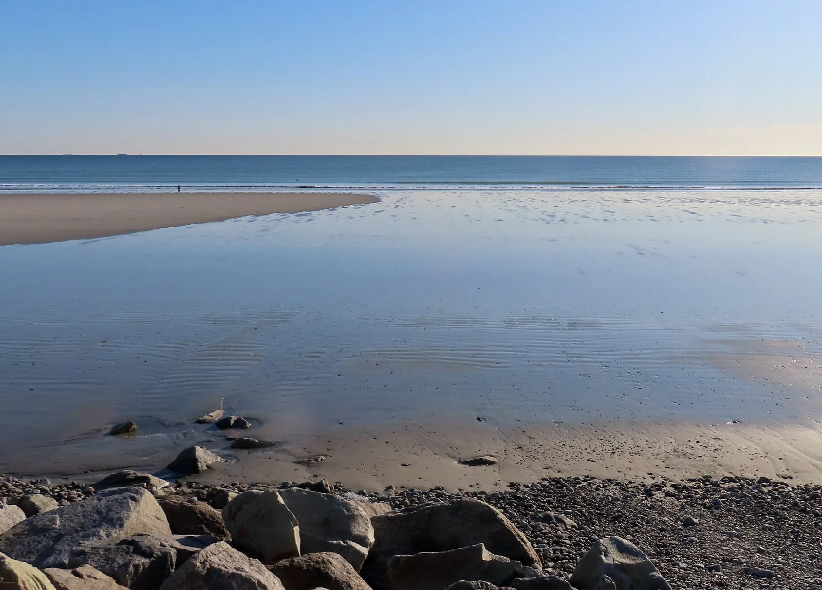 Wet sand and tide pools with the ocean beyond under a pale sky