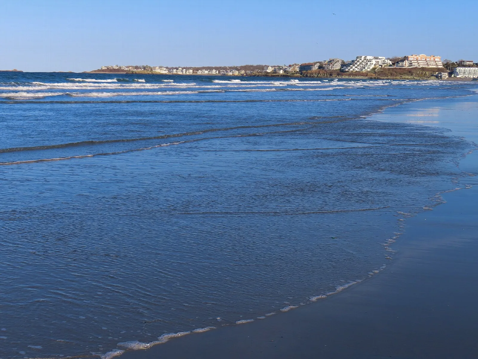 Gentle waves washing a long blue beach toward distant buildings