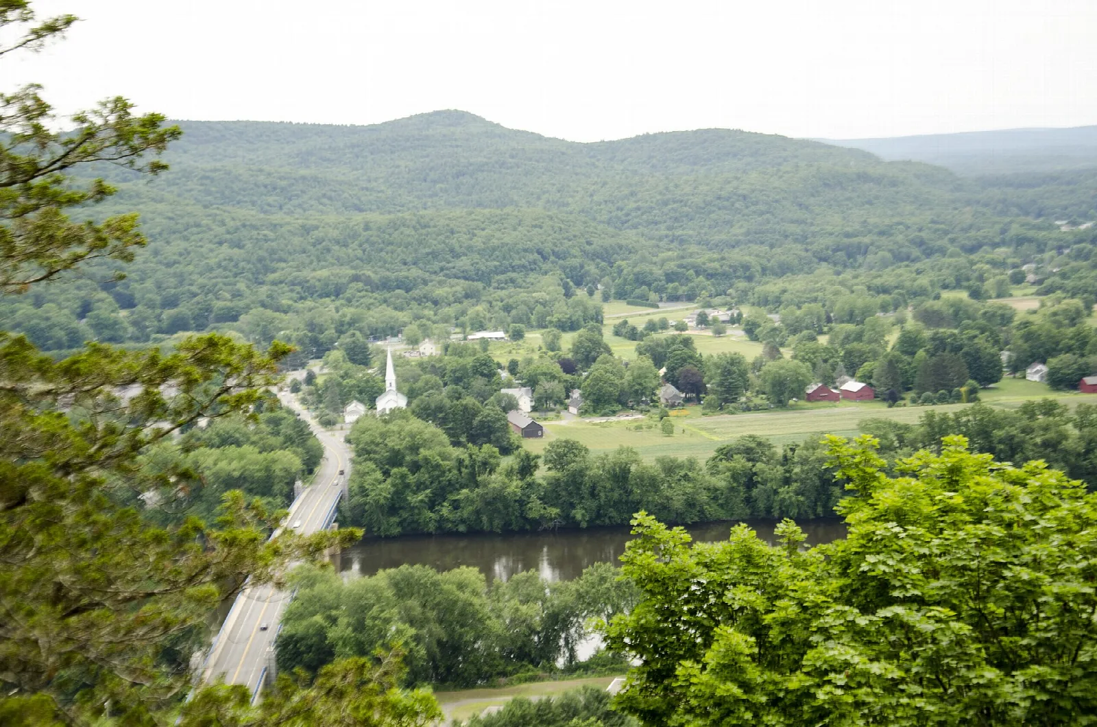 Wooded valley with a bridge and a village below hazy hills