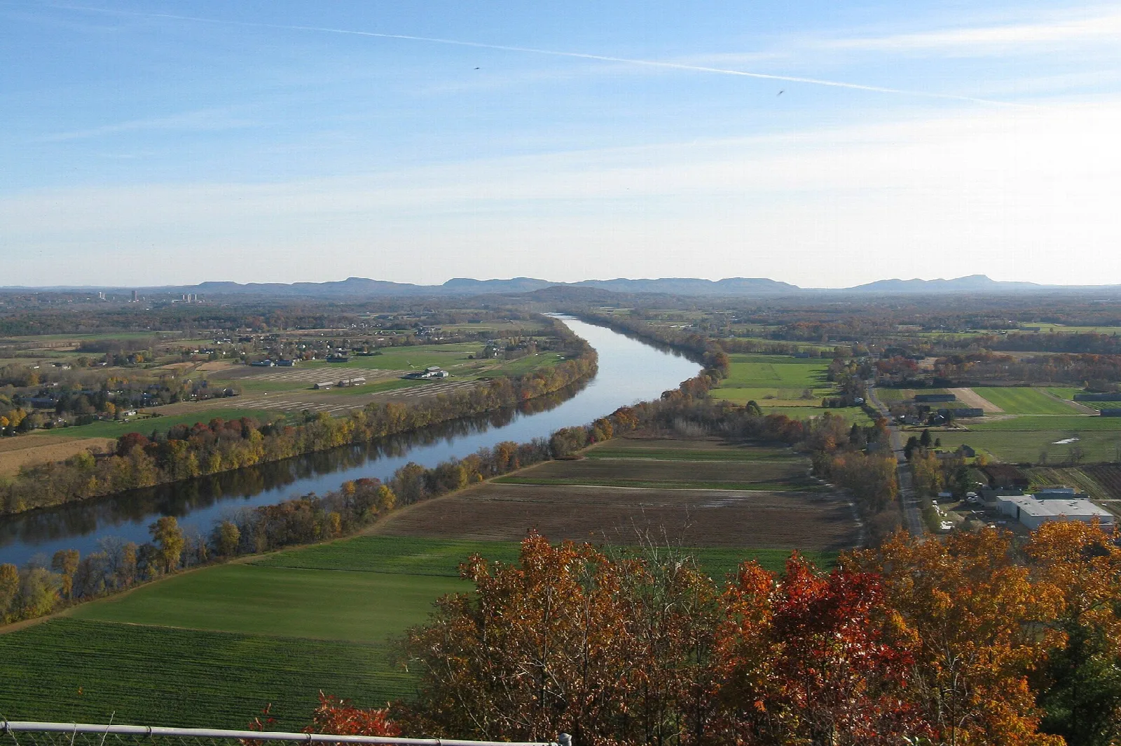River winding through green farm fields and fall trees, seen from a summit