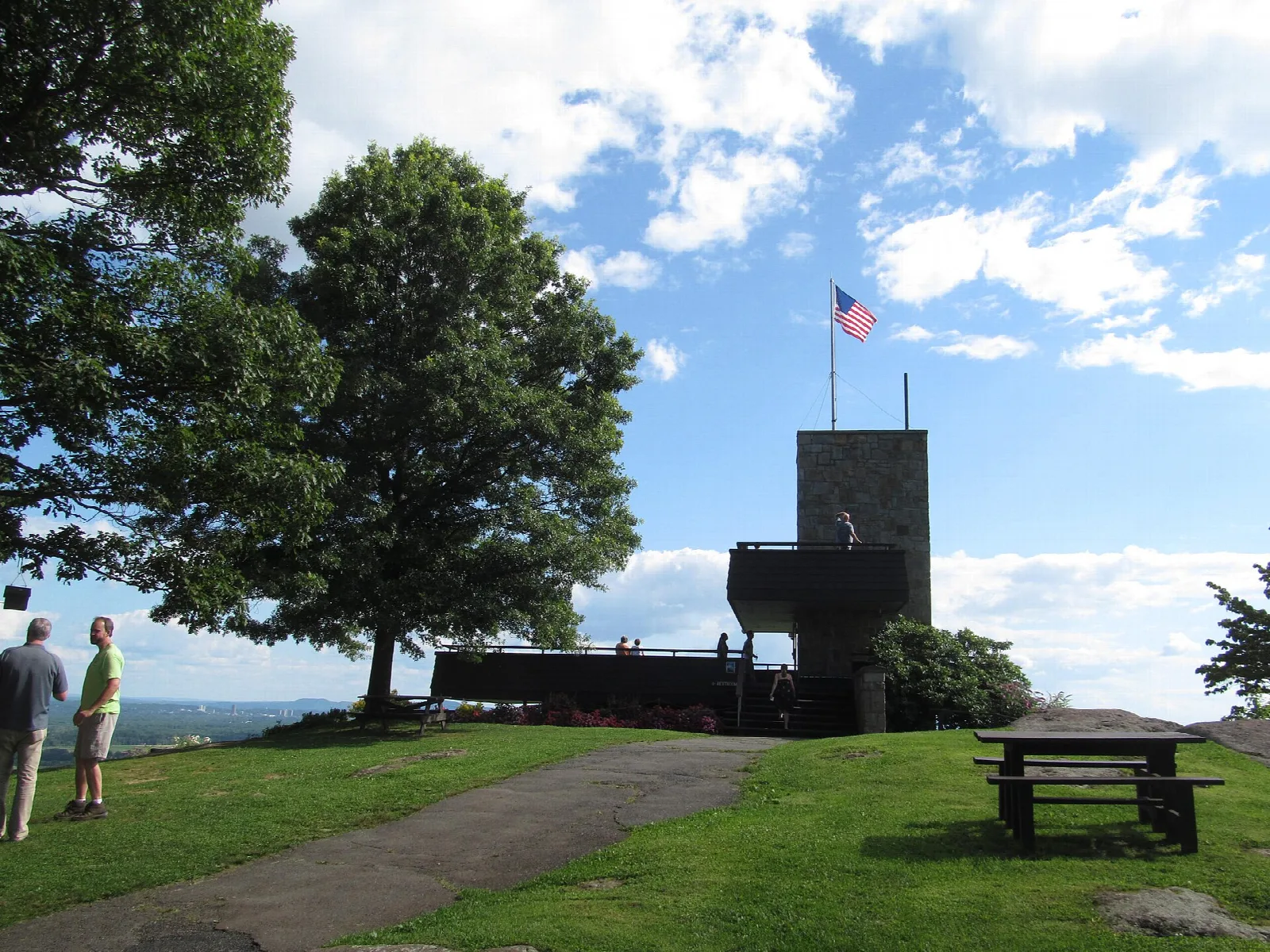 Stone summit tower with a flag, a tree and two people on a lawn