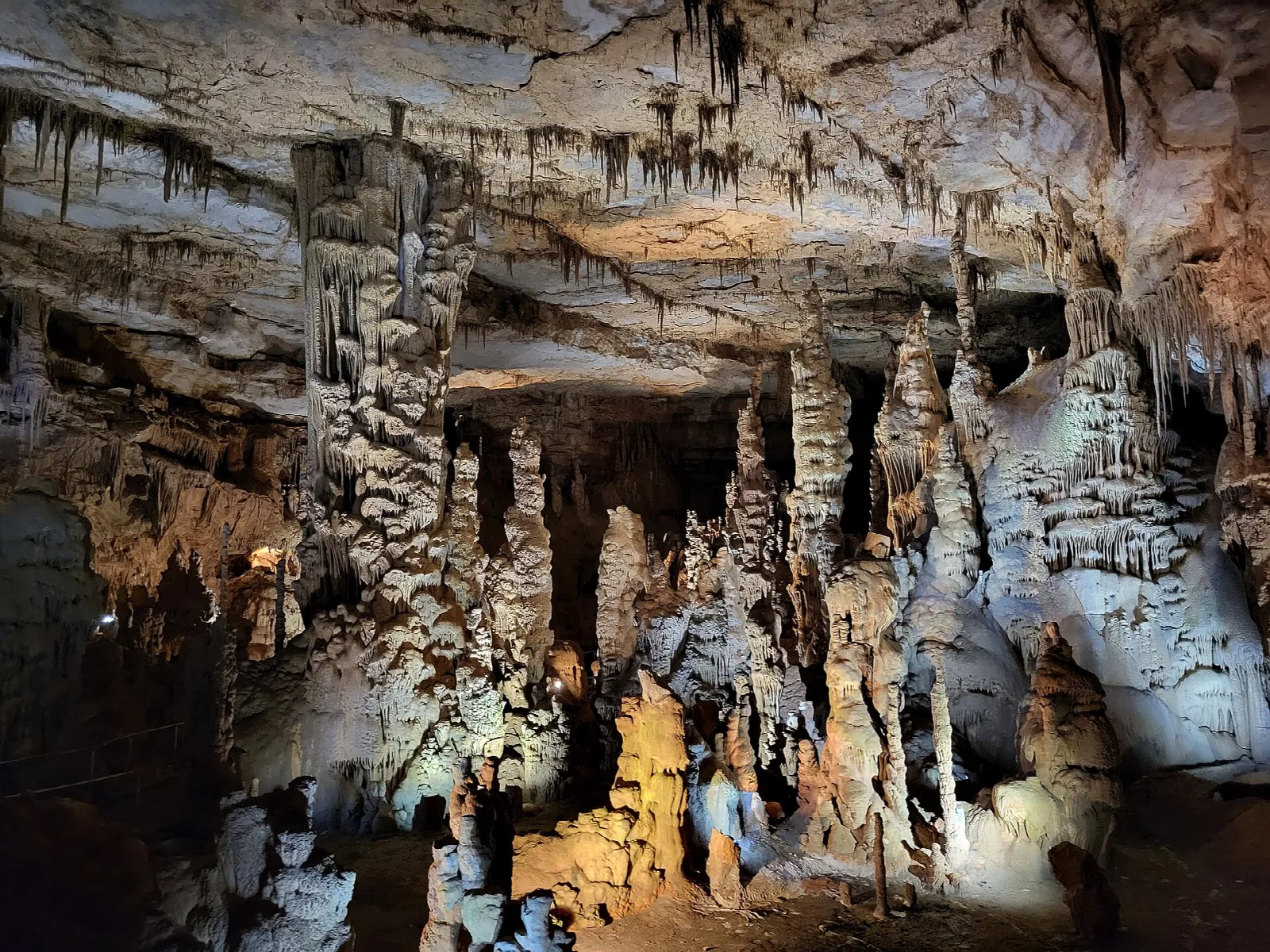 Large cave room with tall stalagmites and a ridged ceiling lit from below
