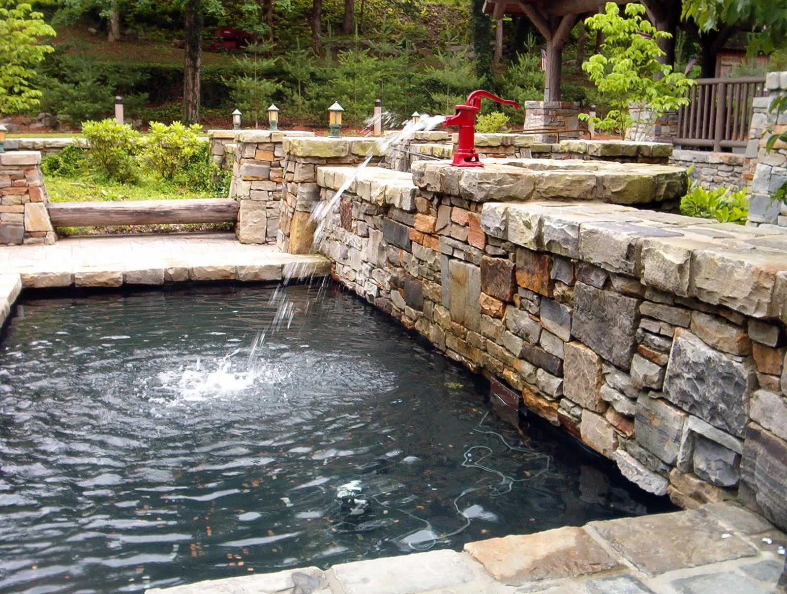 Stone-walled pool with a small fountain and green plantings behind it