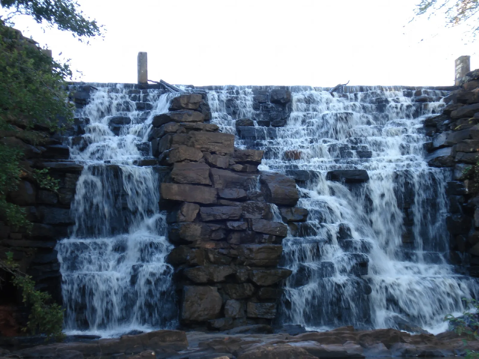 Water spilling down a wide stepped stone dam surrounded by trees