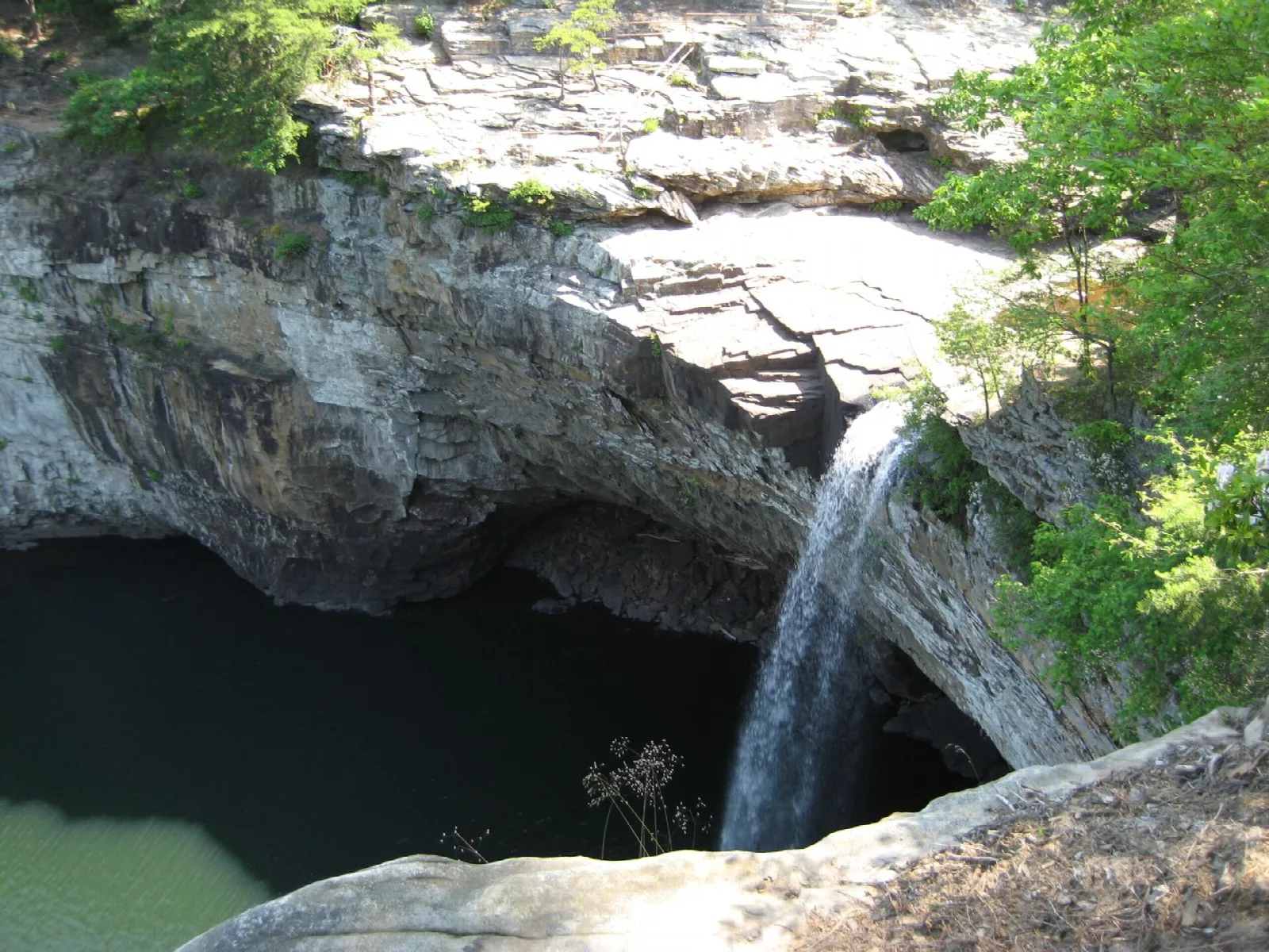 Thin waterfall dropping over a rock ledge into a dark pool