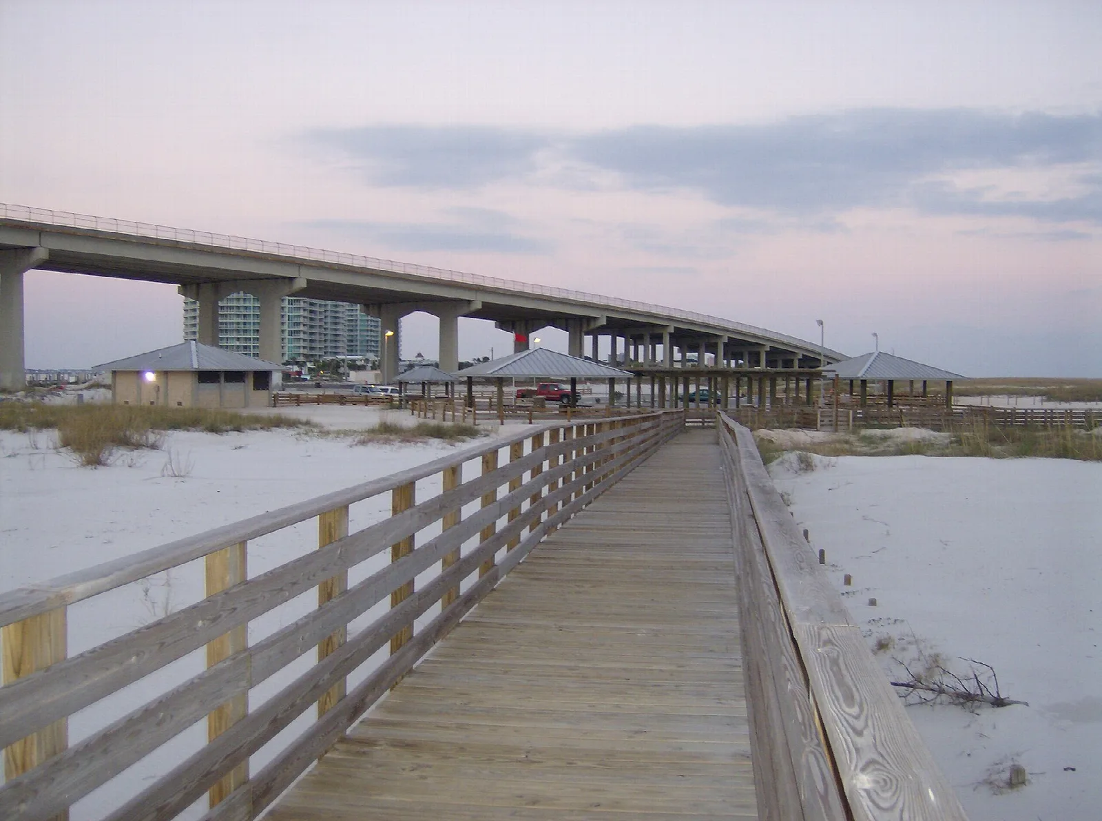 Wooden pier walkway beside a long bridge over water at dusk