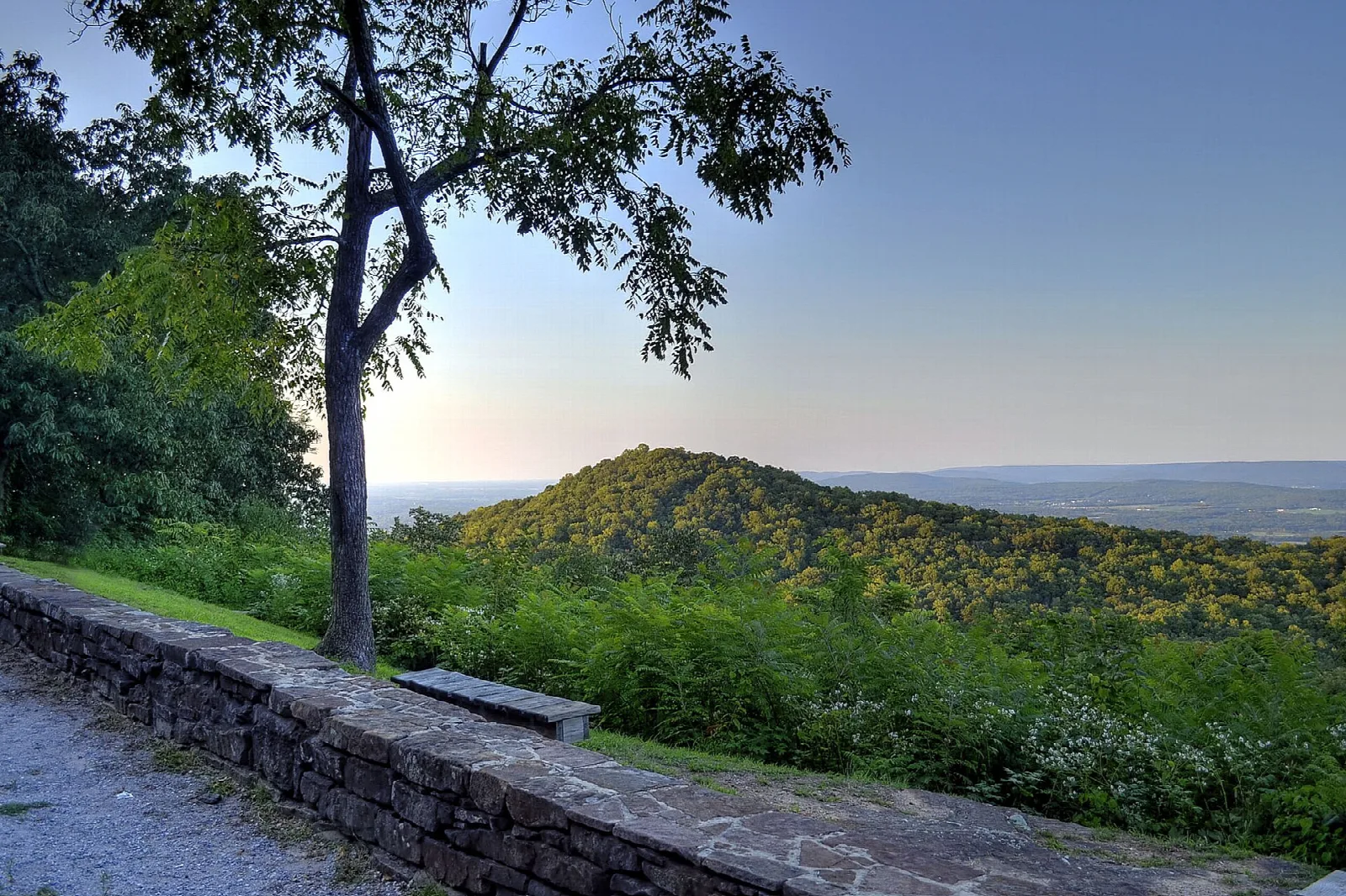 Stone wall along an overlook with a wooded ridge and valley beyond under a blue sky