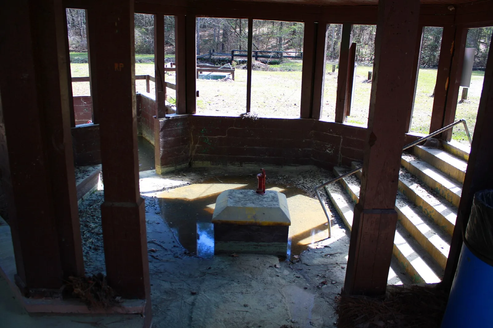 Inside the spring pavilion looking at a stone-edged pool with wooden steps